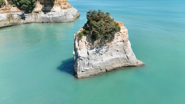 Aerial view of a sea stack with vegetation on top, surrounded by turquoise ocean waters near the coastline of Urenui, Taranaki Region, New Zealand.
