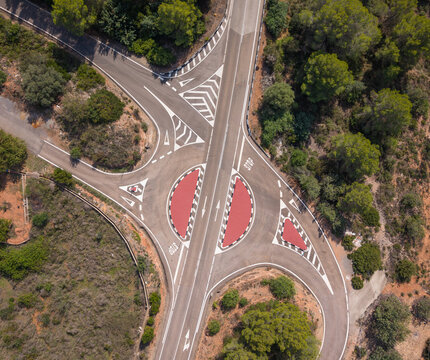 Aerial view of a rural road junction with a small roundabout surrounded by pine trees and dry vegetation in Spain.