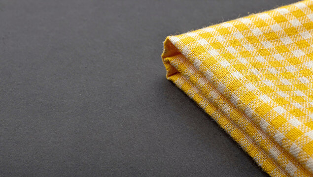A folded yellow and white checkered kitchen towel lies on a dark gray textured background