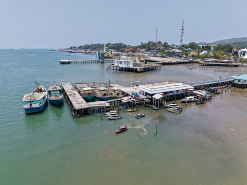 Aerial view of a coastal harbor with various boats docked at wooden piers, small speedboats, and buildings extending over the water in Kotabaru Regency, South Kalimantan, Indonesia.