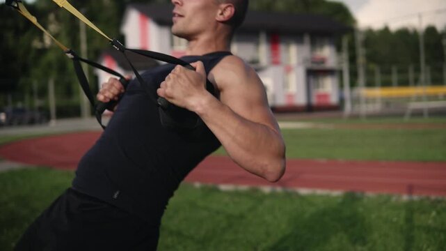 Athletic man doing suspension training for his back and biceps performing rows outdoors at a sports ground on the grass