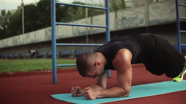 Muscular man performing up-down plank exercise during intense outdoor functional training workout