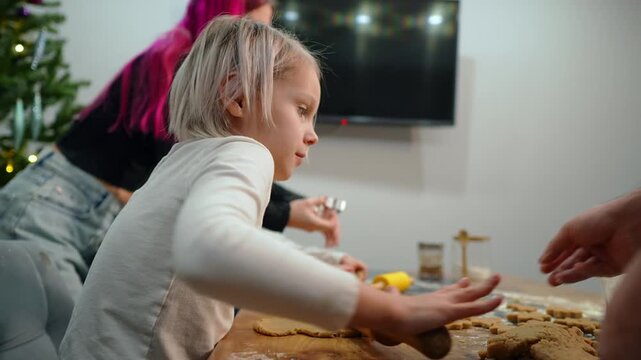Caucasian happy family gathering in the kitchen to make Christmas cookies together. Daughter kneads dough and father cut shaped biscuits. Parenting and passing down cherished traditions concept