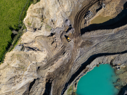Aerial view of a quarry with a yellow bulldozer, excavated earth, and a turquoise water-filled pit in Rathmore, County Kildare, Ireland.