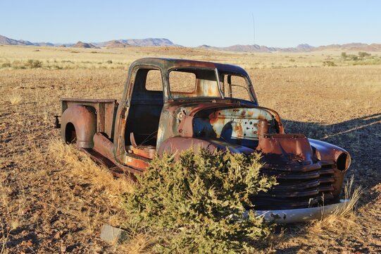 Scrap vehicle at the edge of the desert, Naukluft Mountains at back, Republic of Namibia, Africa
