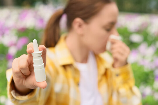 Seasonal allergy relief, woman holding nasal spray with hay fever symptoms in a blooming flower garden during spring pollen season for health care