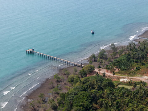 Aerial view of Gedambaan pier extending into the sea, with a boat nearby, surrounded by lush tropical vegetation and sandy coastline in Pulau Laut Utara, South Kalimantan, Indonesia.