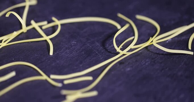 Close-up of uncooked thin noodles scattered on a dark textured background, pieces of dry vermicelli on black slate