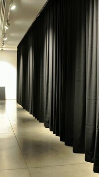 Vertical video: Pushing camera moving forward in gallery, showing long black curtain, pedestal