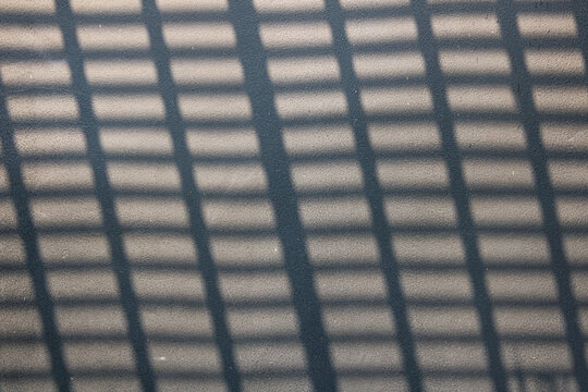 A textured, grainy surface with parallel and cross-hatched shadow patterns cast across it.
