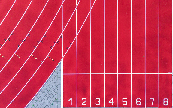 Aerial view of a red running track with white lane markings and numbered lanes from one to eight, featuring a paved corner section. The Netherlands.