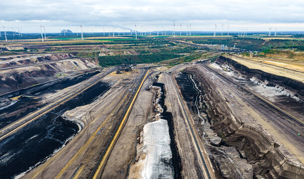 Aerial view of the Garzweiler surface mine showing open-pit coal mining operations, deep excavation terraces, and wind turbines on the horizon in Juchen, North Rhine-Westphalia, Germany.