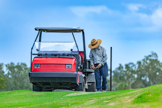 Golf Course Groundskeeper Repairing Turf Divots Next to Red Utility Vehicle on Fairway
