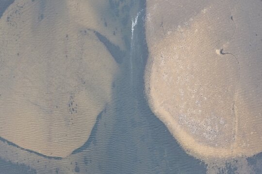 Aerial view of the sandy shorelines and calm waters of Lake Estes, featuring textured sediment patterns and natural landscape features in Estes Park, Colorado, United States.