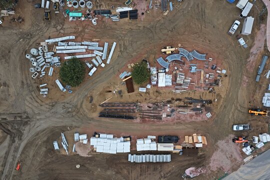 Aerial view of a construction site featuring stacks of building materials, pipes, and heavy machinery on a dirt lot in Estes Park, Colorado, United States.