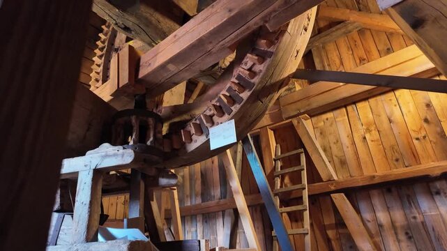 Slow camera movement across a large wooden wheel powering an antique flour mill, highlighting historic mechanical engineering, traditional craftsmanship and rural industrial heritage.
