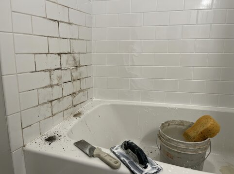 Worker regrouting tile around a bathtub