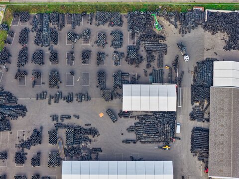 Aerial view of a large tire recycling and storage facility with organized stacks of used tires, industrial warehouses, and loading areas in Hombourg, Grand Est, France.
