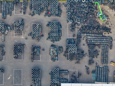 Aerial view of a large outdoor storage yard filled with organized stacks of used tires and a green crane in Hombourg, Grand Est, France.