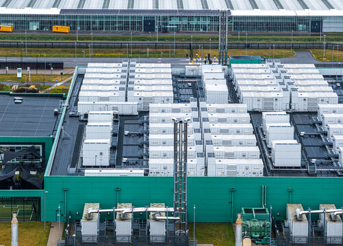 Aerial view of Agriport A7 industrial facility featuring numerous white cooling units on the roof, green exterior walls, and large greenhouse structures in Middenmeer, Noord-Holland, Netherlands.