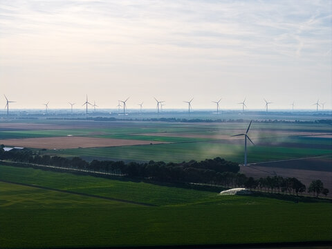 Aerial view of the Agriport A7 wind farm featuring numerous wind turbines set against vast agricultural fields and a hazy horizon in Middenmeer, Noord-Holland, Netherlands.