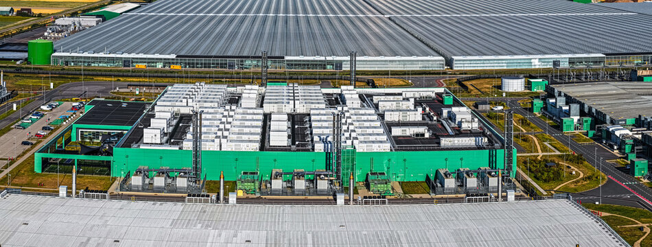 Aerial view of Agriport A7, an industrial facility with green walls and white cooling units, surrounded by vast greenhouse complexes in Middenmeer, Noord-Holland, Netherlands.