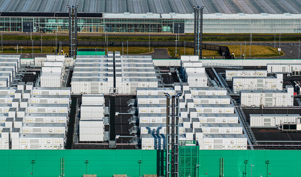Aerial view of Agriport A7 facility with rows of white cooling units, a large green wall, and glass greenhouses in the background in Middenmeer, Noord-Holland, Netherlands.