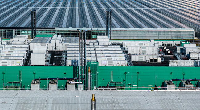 Aerial view of Agriport A7 industrial facility featuring rows of white technical units, green walls, and large glass greenhouses in Middenmeer, Noord-Holland, Netherlands.