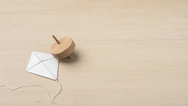 Plain wooden spinning top and blank paper kite on a pale wood floor