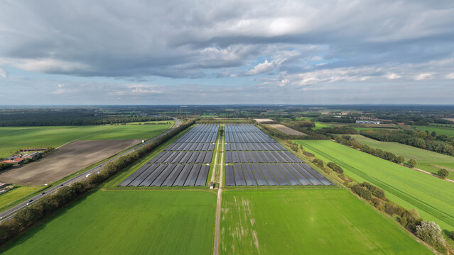 Aerial view of a large solar park with rows of photovoltaic panels situated in a green rural landscape with a highway nearby in The Netherlands.
