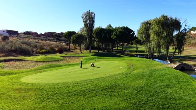 Professional golfers playing on a beautiful green with a sand bunker and a small river
