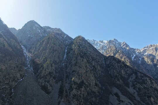 Aerial view of the rugged Caucasus mountains with steep rocky slopes, patches of snow, and deep valleys in Dariali, Mtskheta-Mtianeti, Georgia.