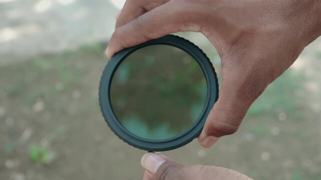 Close up of photographer hands holding dark circular variable ND filter adjusting density with lever outdoors