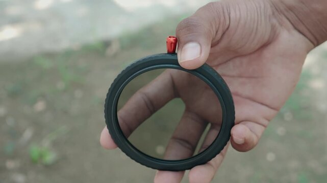 Close up of photographer hand holding variable neutral density ND filter showing stop markings and red lever