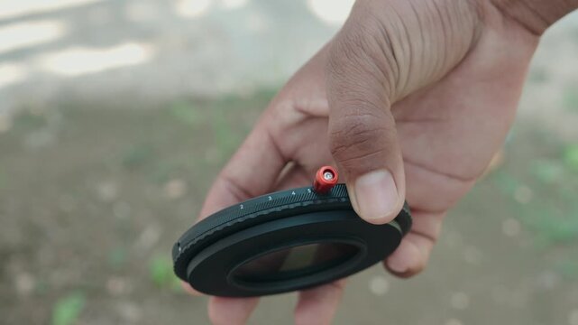 Close up of photographer hand holding variable neutral density ND lens filter with red control lever outdoors