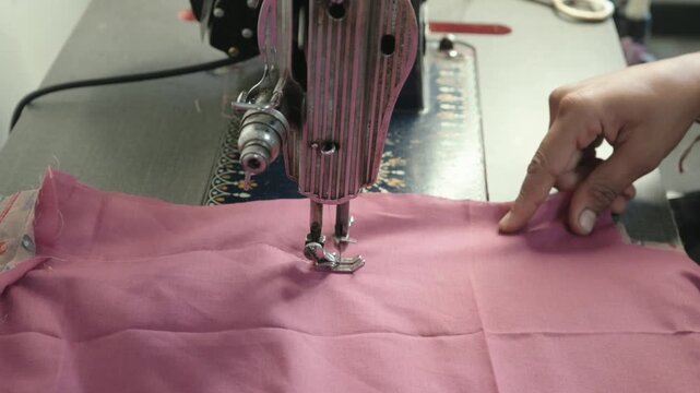 Close up of tailor stitching pink fabric cloth using vintage sewing machine in textile workshop