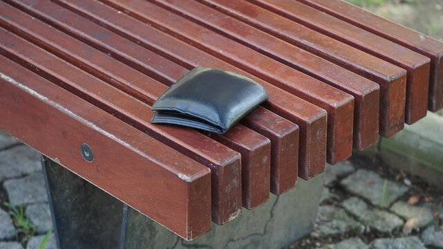 Black wallet resting on a wooden park bench during the day. lost wallet concept 