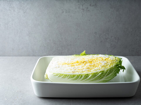 Fresh raw napa cabbage salted with coarse sea salt crystals in a white ceramic tray