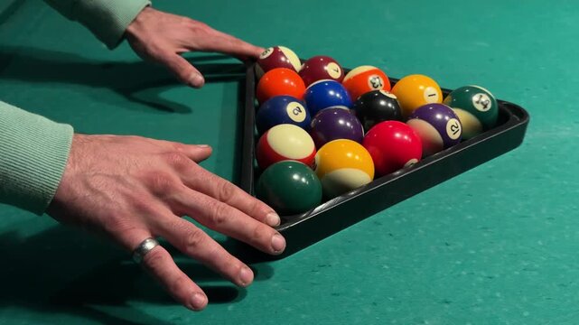 Pool player slides a triangle rack filled with billiard balls away from the cushion, positions the balls for the opening break and removes hands from the table, close-up setup, horizontal video