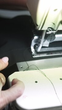 Vertical video. Sewing machine work. Tailor process. Female hand stitching garment buttonhole of black clothing on electrical equipment in workshop.
