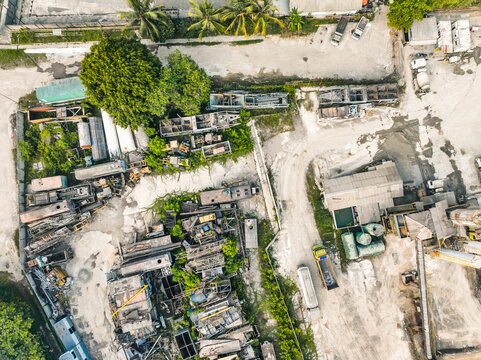 Aerial view of an industrial site featuring heavy machinery, trucks, storage buildings, and surrounding vegetation in Klapanunggal, West Java, Indonesia.