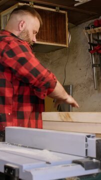 Vertical video. Professional carpentry. Lumber craft. Male joiner preparing smoothed plank for diy project in carpentry equipped with tools.