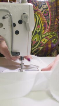 Vertical video. Tailor work. Custom garment. Female hand attaching lace to white textile clothes on professional electrical stitching equipment.