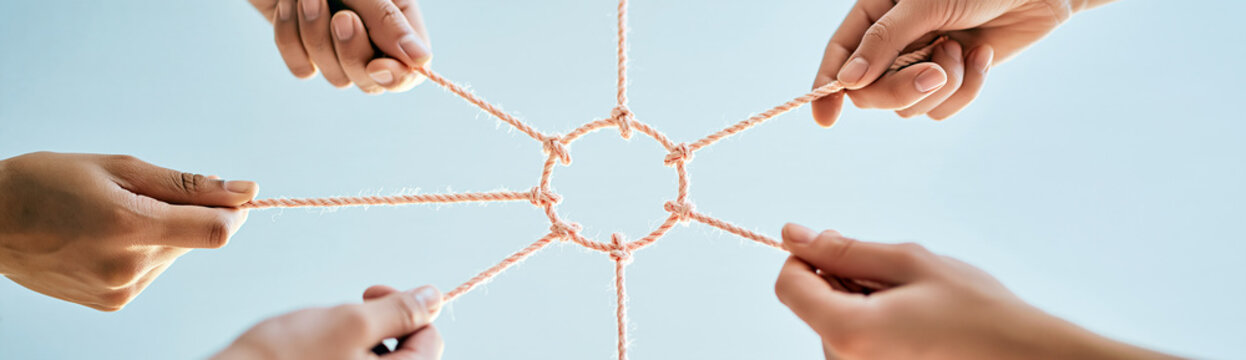 Six hands holding ropes connected at the center, symbolizing teamwork and collaboration against a clear sky background.