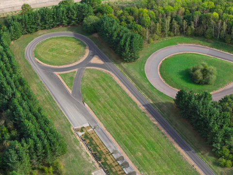 Aerial view of a vehicle testing track with circular asphalt roads surrounded by lush green grass and dense forest in the United Kingdom.