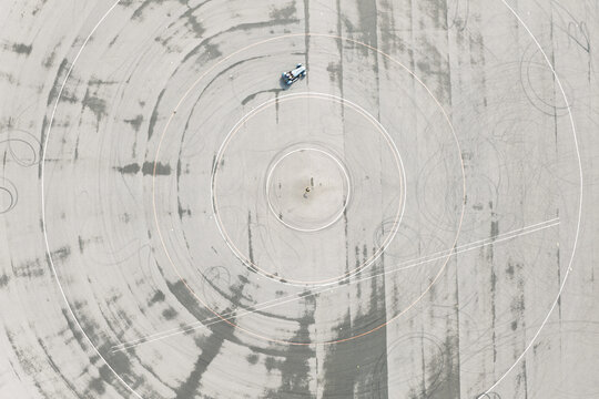 Aerial view of a car performing circular maneuvers on a test track, leaving tire marks on the asphalt surface in the United Kingdom.