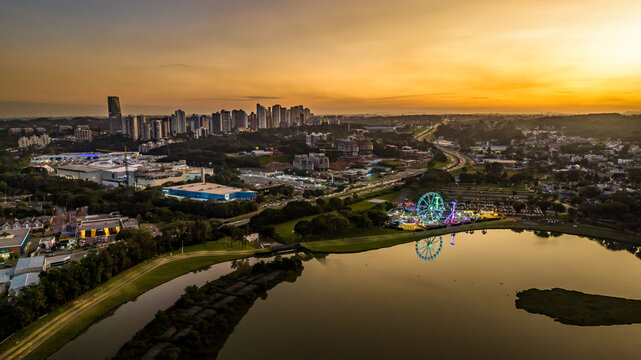 Aerial view of the Curitiba skyline at sunset, featuring a lake with a glowing ferris wheel and amusement park, surrounded by urban buildings and greenery in Curitiba, Parana, Brazil.