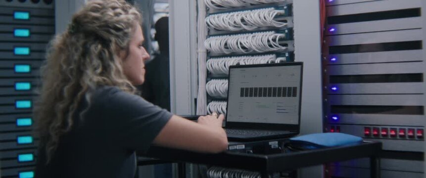 Female System Administrator Analyzing Server Performance Metrics on Laptop. IT Infrastructure Monitoring, Cloud Resource Management, Enterprise System Diagnostics, and Digital Operations Control.