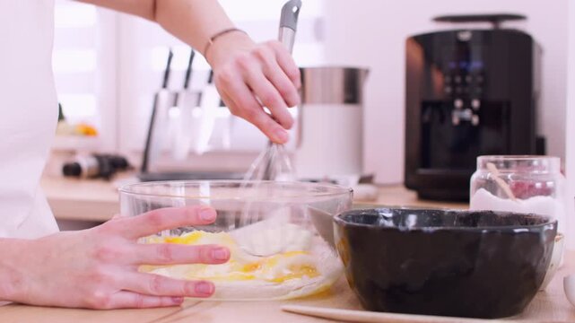 Dessert making. Whisking process. Woman baker hand mixing sugar cream egg yellow batter for homemade dough in glass bowl on table.