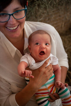 Smiling Mother Holding a Surprised Baby in Colorful Striped Pants